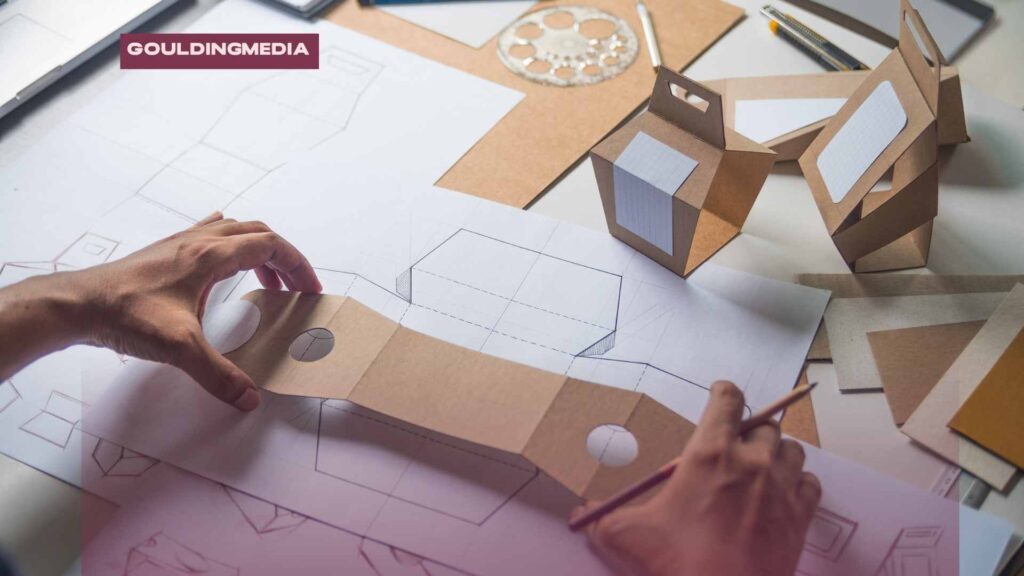 Person sketching and assembling cardboard packaging prototypes on a table.