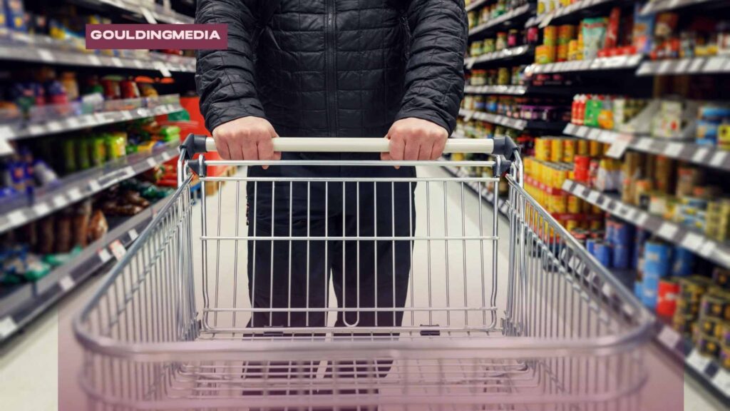 Shopper pushing a trolley through a supermarket aisle filled with packaged food products.