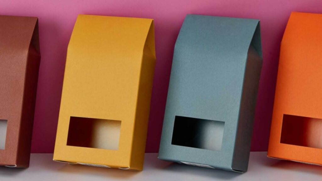 Vibrant die-cut folding cartons in red, yellow, teal, and orange, lined up against a pink background.