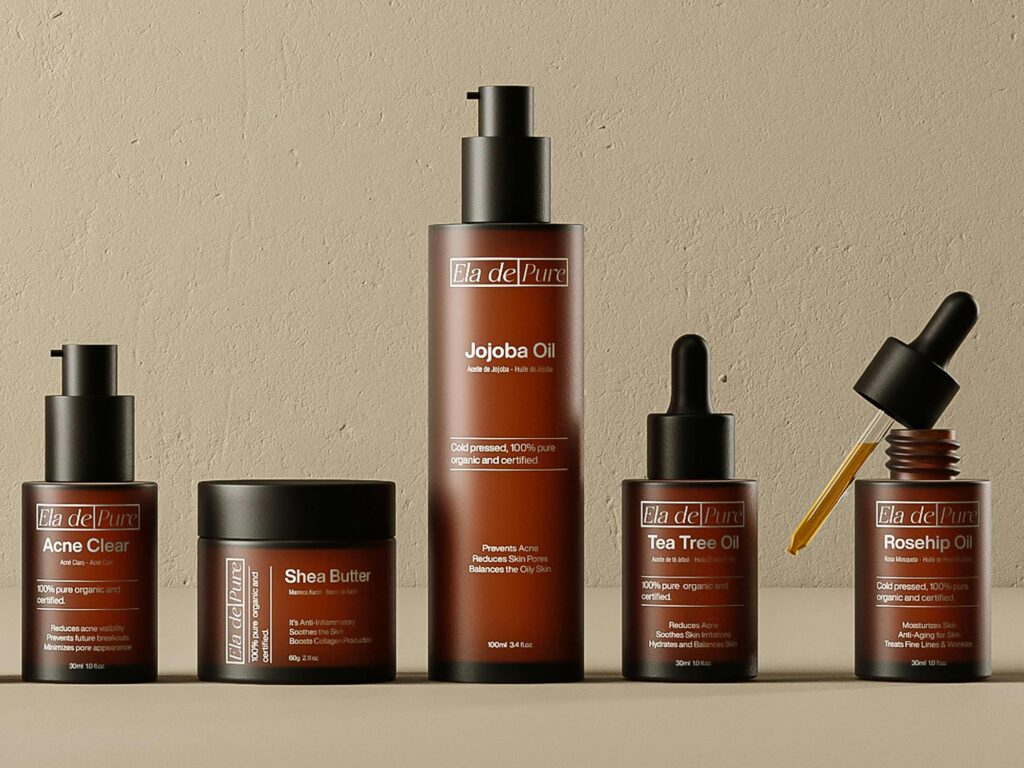 ELA DE PURE skincare products in amber-toned bottles with pump and dropper designs, arranged against a beige backdrop.