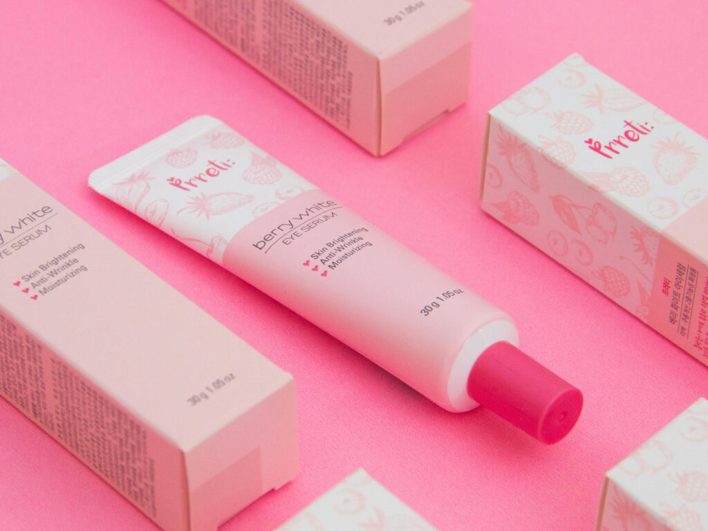 Prreti Berry White Tone-Up Cream in a pink tube with coordinating boxes, set against a bright pink background.