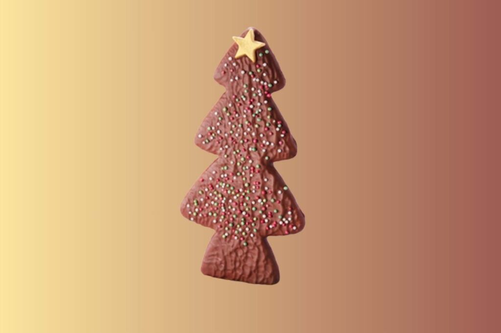Chocolate tree-shaped biscuit with sugar decorations on gold gradient background.