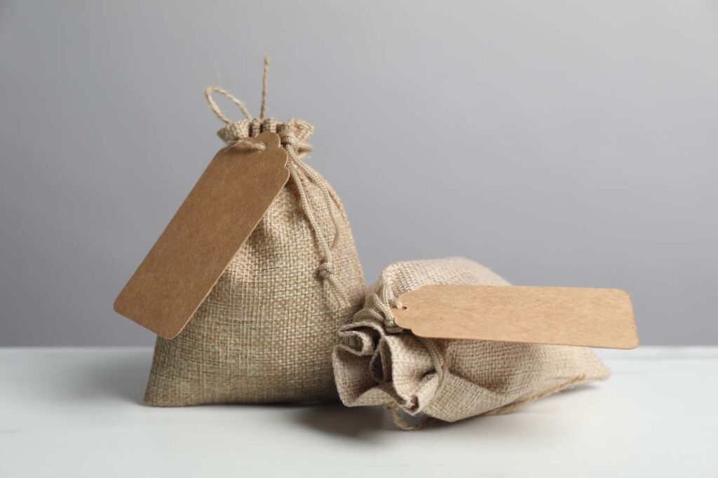 Natural jute bags with drawstrings and kraft tags on a neutral background.