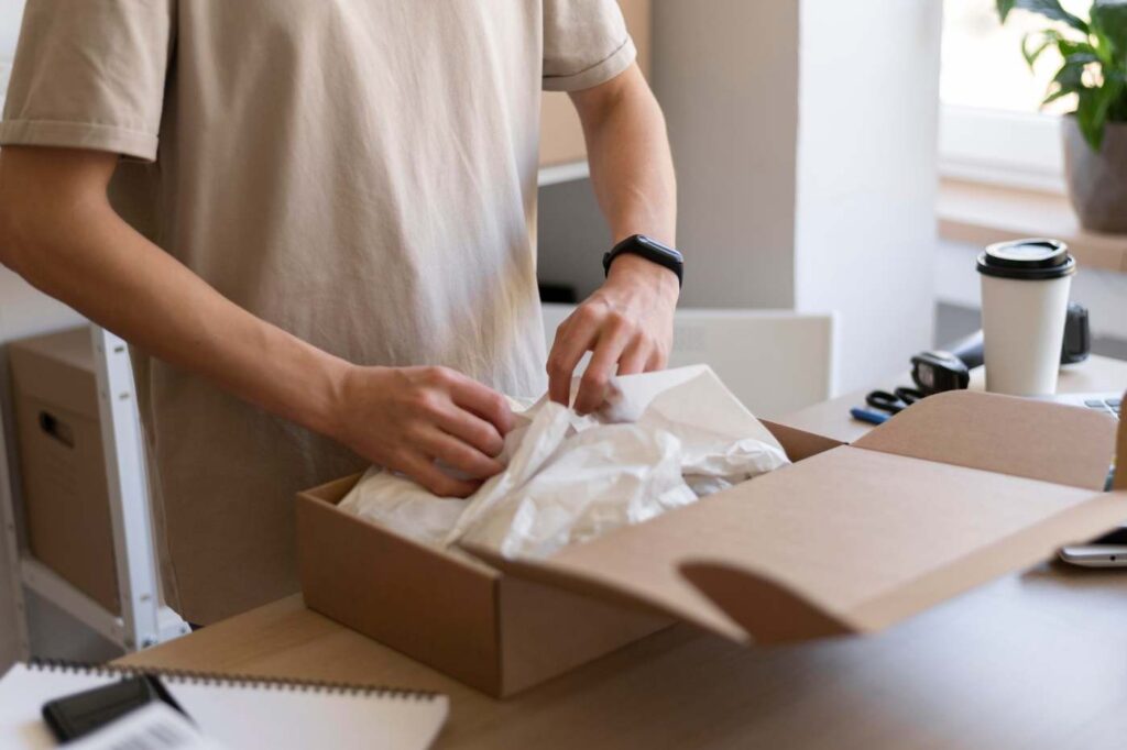 Person filling a cardboard box with tissue-style filler and protective packing materials