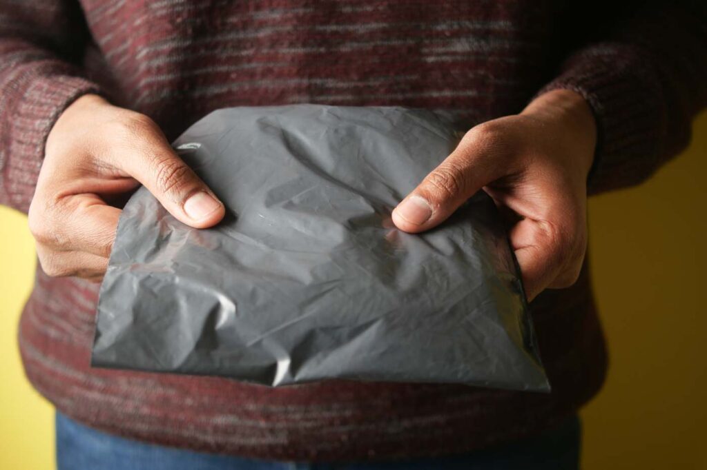 Person sealing a grey poly mailer with product inside.