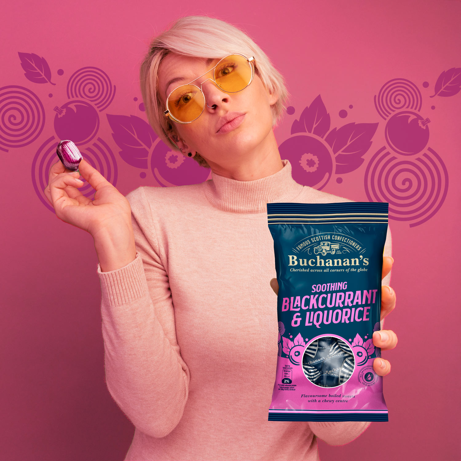 Young woman holding Buchanan’s Blackcurrant and Liquorice sweets in modern packaging against pink background