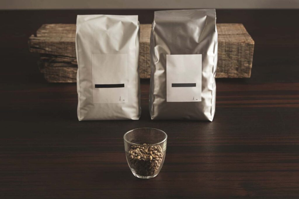 Two matte foil stand-up pouches with a small glass jar of coffee beans in front.