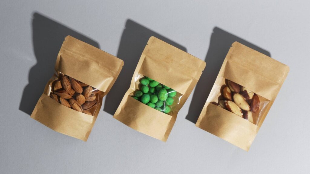 kraft paper pouches open to reveal almonds and green-coated nuts, arranged with shadows.