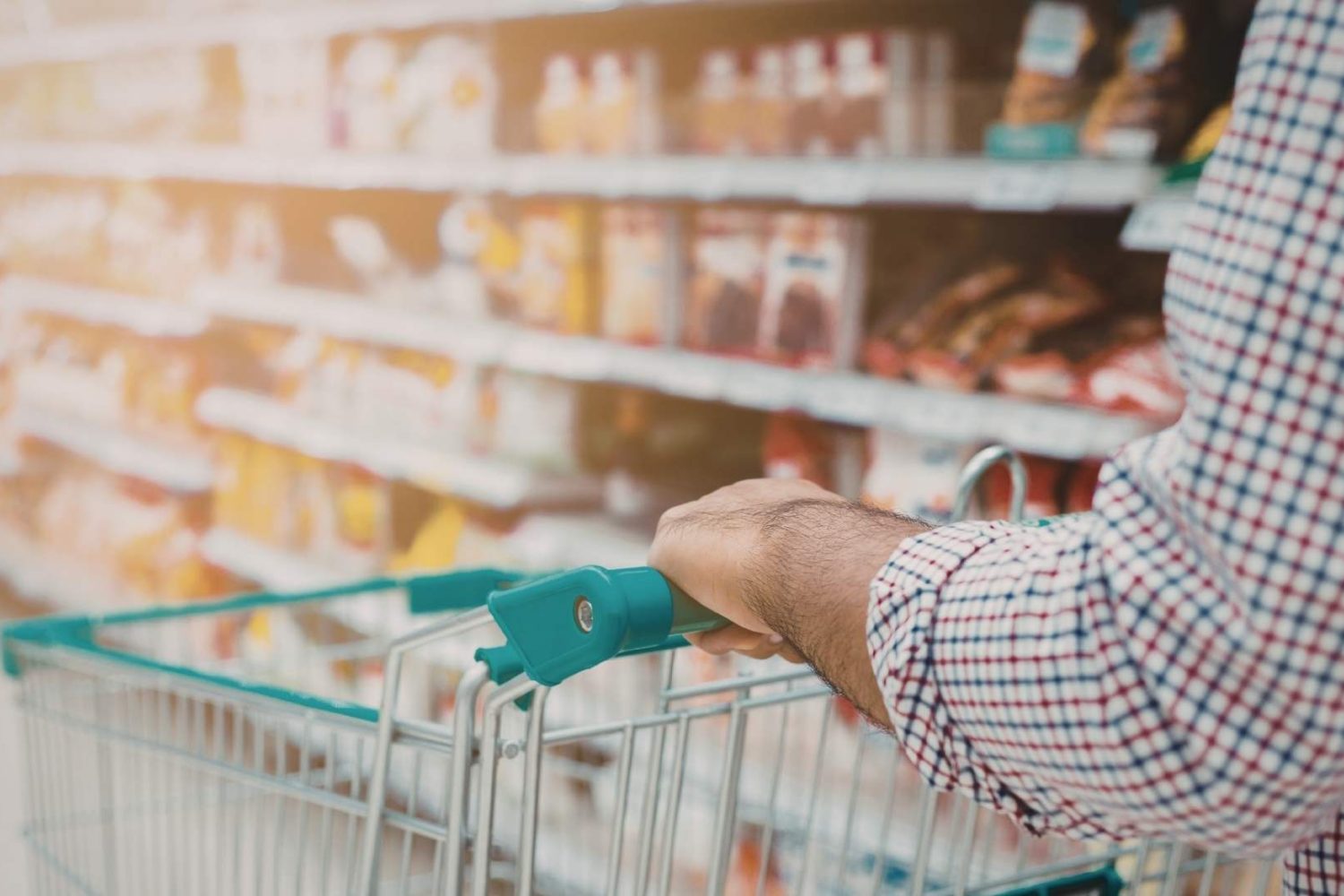 Person pushing a shopping trolley through a supermarket aisle, browsing packaged food.