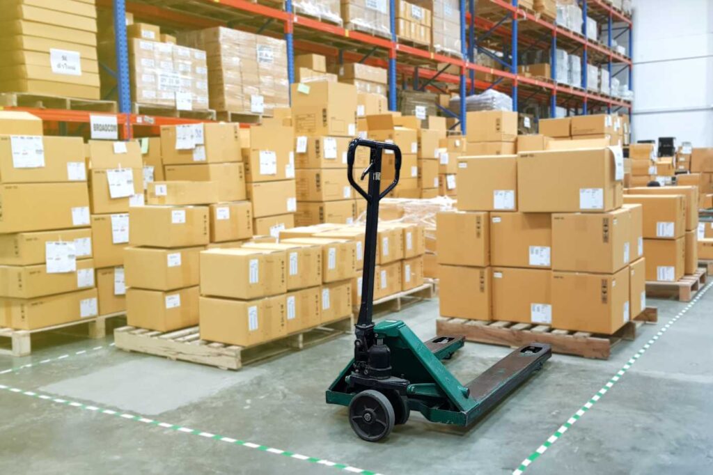 A warehouse scene with numerous cardboard boxes and a pallet jack in the center.