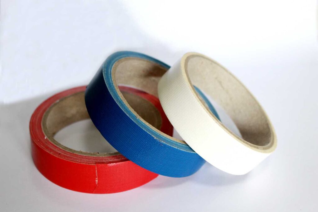 Three rolls of colored adhesive tape (red, blue, and white) placed on a white surface.